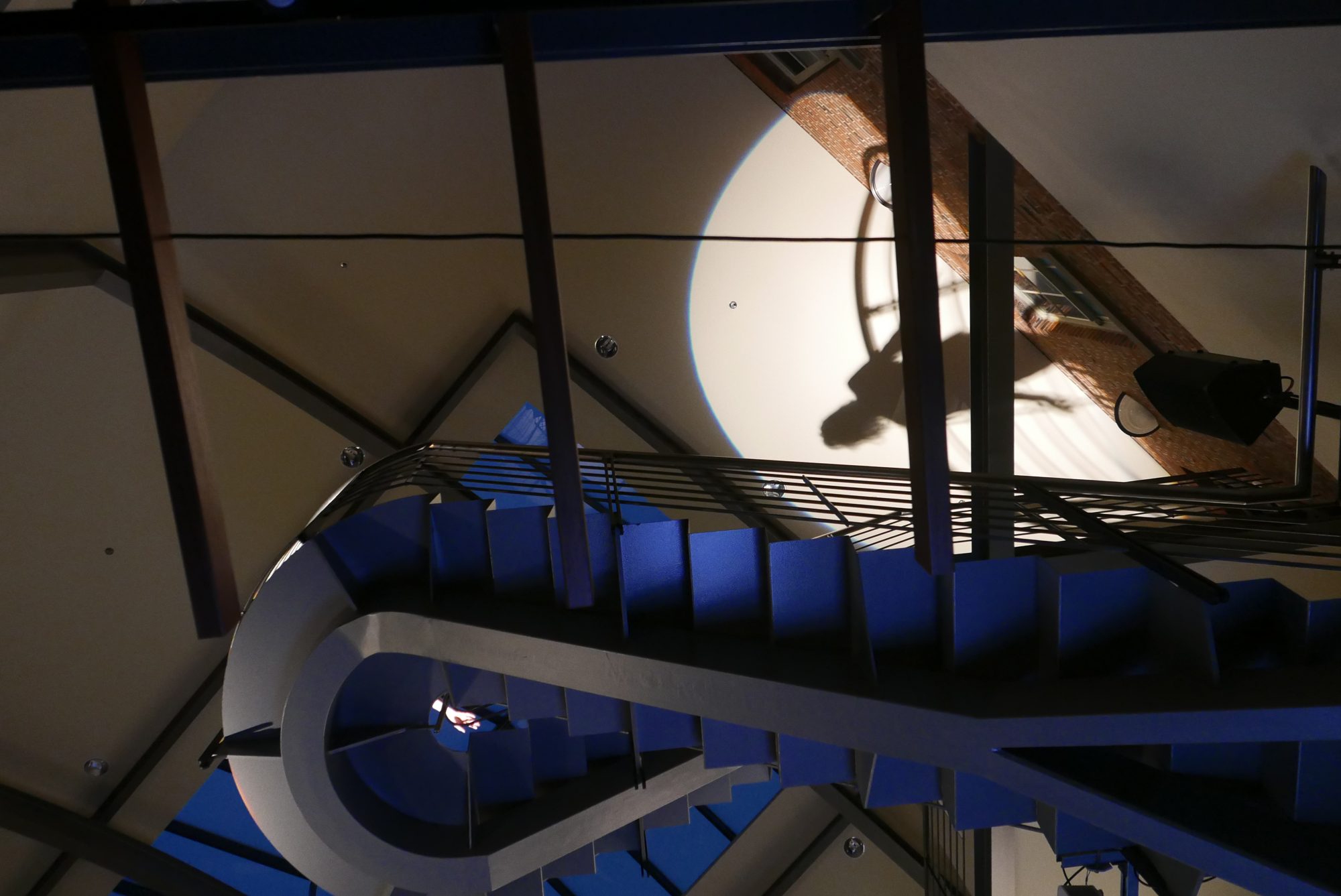 The curving atrium staircase lit by a circle of light, seen from below