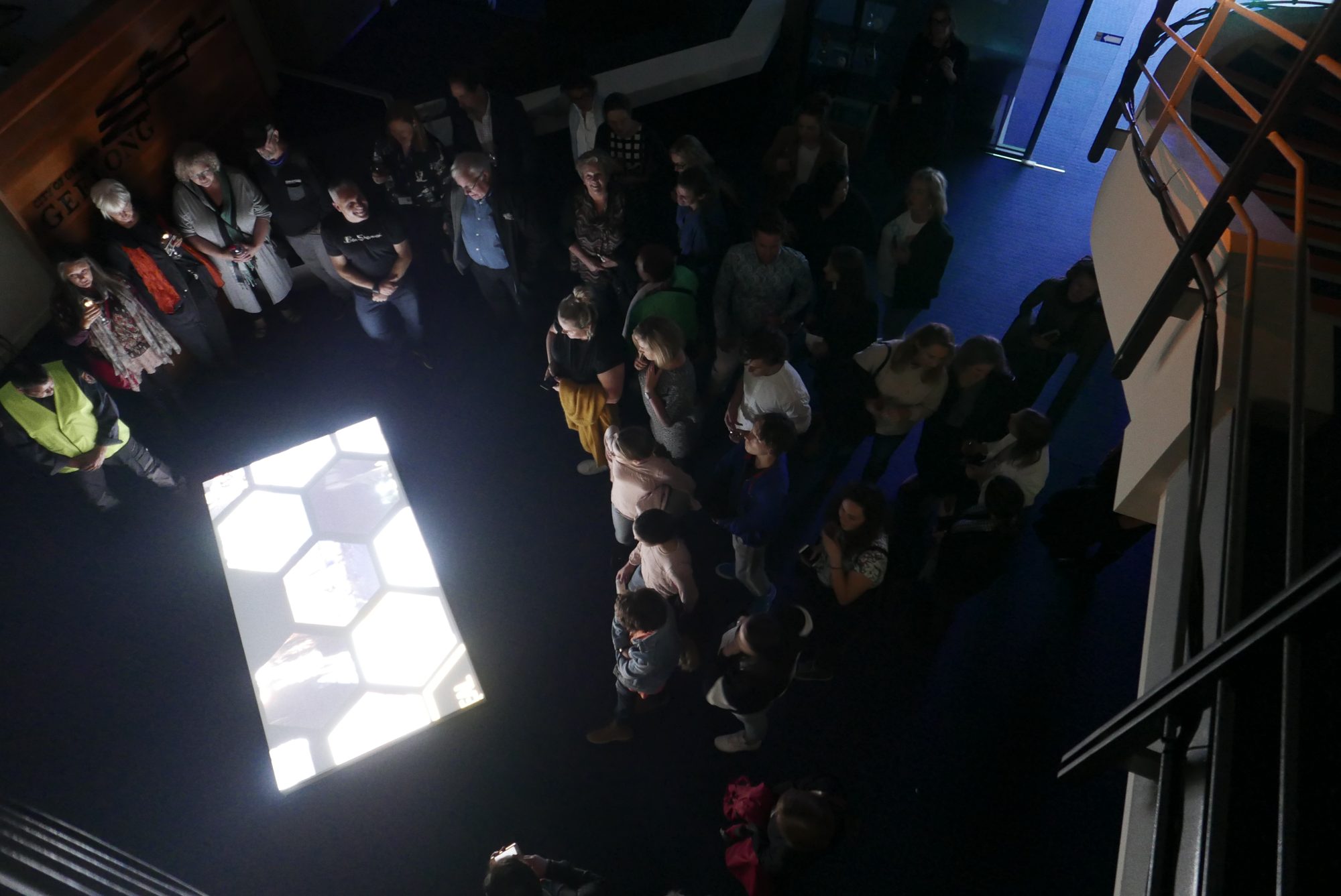 Visitors gathered round a projected honeycomb of Beehive videos on the atrium floor, seen from above