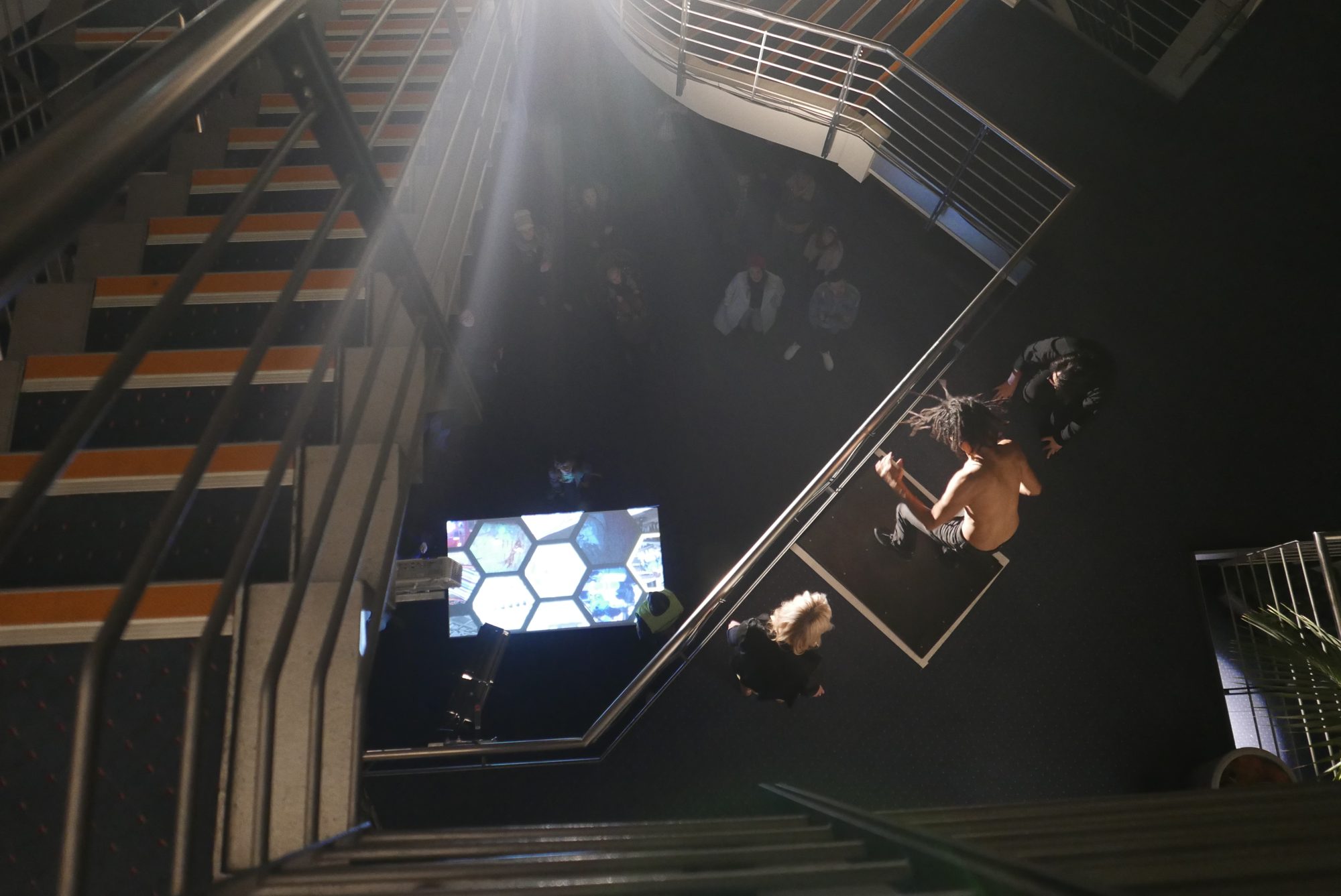 Looking down the atrium stairwell to performers and the projected Beehive feed