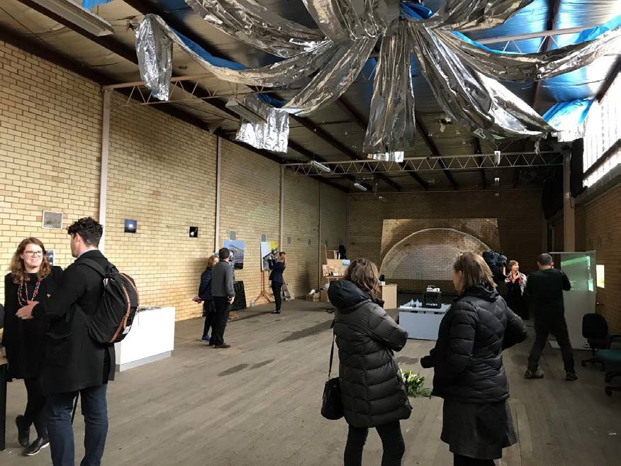 Visitors in the exhibition hall of the National Wool Museum under a hanging silver ceiling work